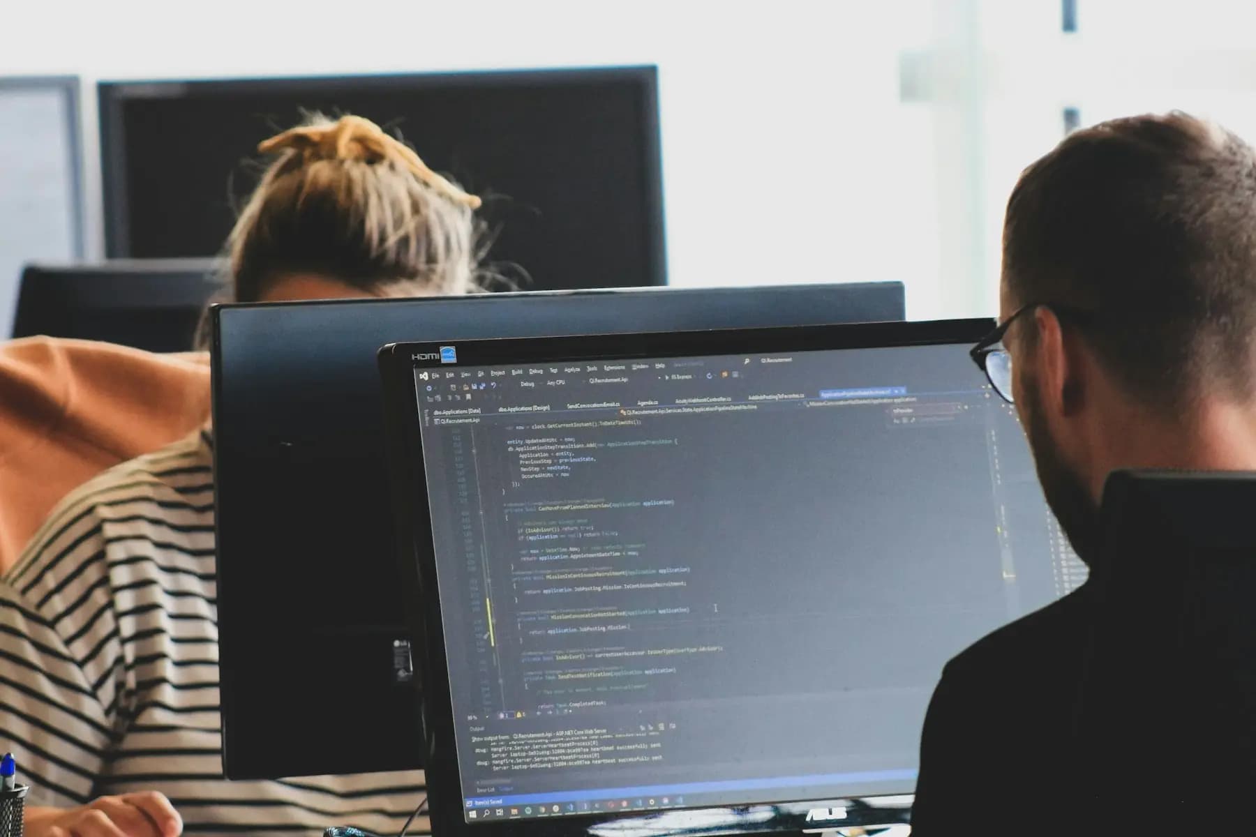 Two people at work on code, seen from behind their monitors.